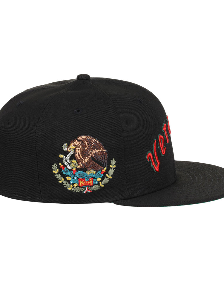 The EFF Veracruz Azules NLB Team Color Fitted Ballcap is a black hat with red cursive text on the front panel and an embroidered Mexican coat of arms on the side.