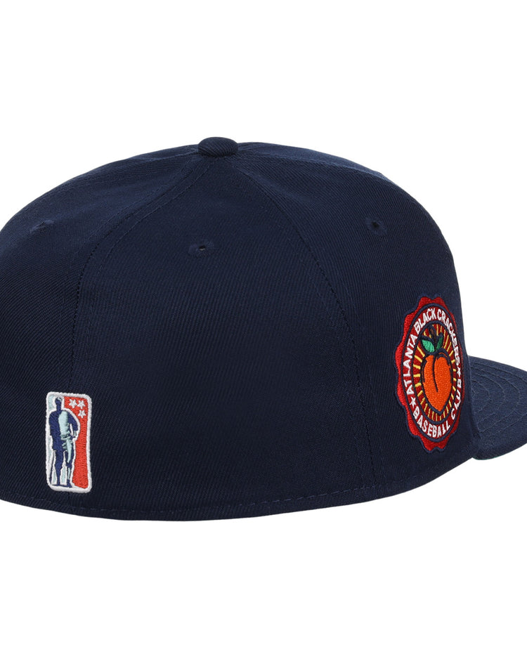 The EFF Atlanta Black Crackers NLB Team Color Fitted Ballcap is a vintage-inspired navy hat with a round orange and green side patch and a small man-with-bat embroidered logo on the back.