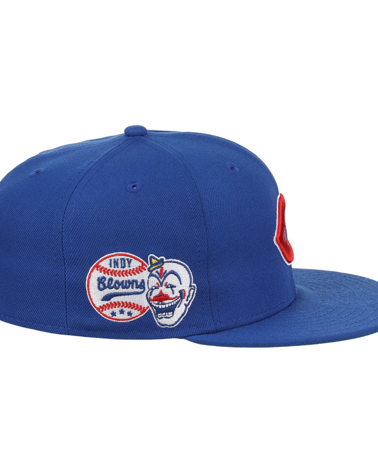 The EFF Indianapolis Clowns NLB Team Color Fitted Ballcap is a blue vintage-inspired cap with side patches—a baseball labeled INDY Browns and a smiling face with a red hat—honoring the Negro American League’s Clowns, plus a bold red C on the front.