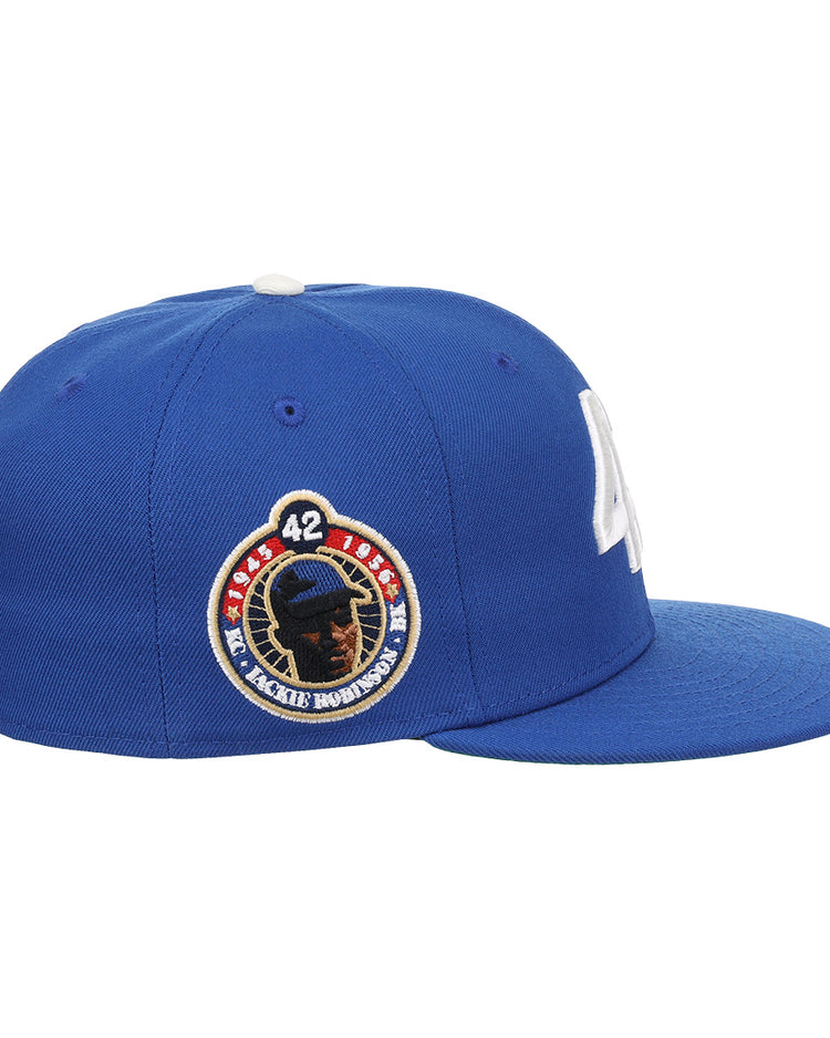 The EFF Jackie Robinson EFF Signature Series Fitted Ballcap - Royal features a blue design with a white button, white embroidered “LA” on the front, and a side patch with Jackie Robinson’s silhouette and number 42.