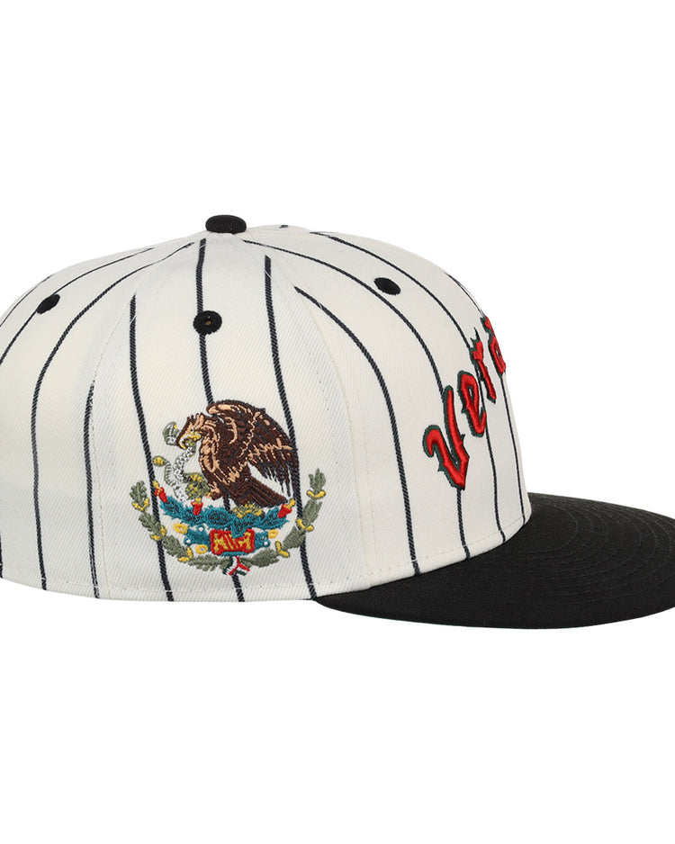 The EFF Veracruz NLB Pinstripe Fitted Ballcap features white fabric with black pinstripes, a black brim, side embroidery of the Mexican coat of arms, and partially visible red letters on the front.