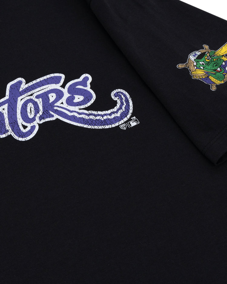 Close-up of the black Norwich Navigators EFF MiLB Vintage T-Shirt by Ebbets Field Flannels, featuring “Gators” in purple and white script on the front and a small cartoon alligator swinging a bat on the sleeve.