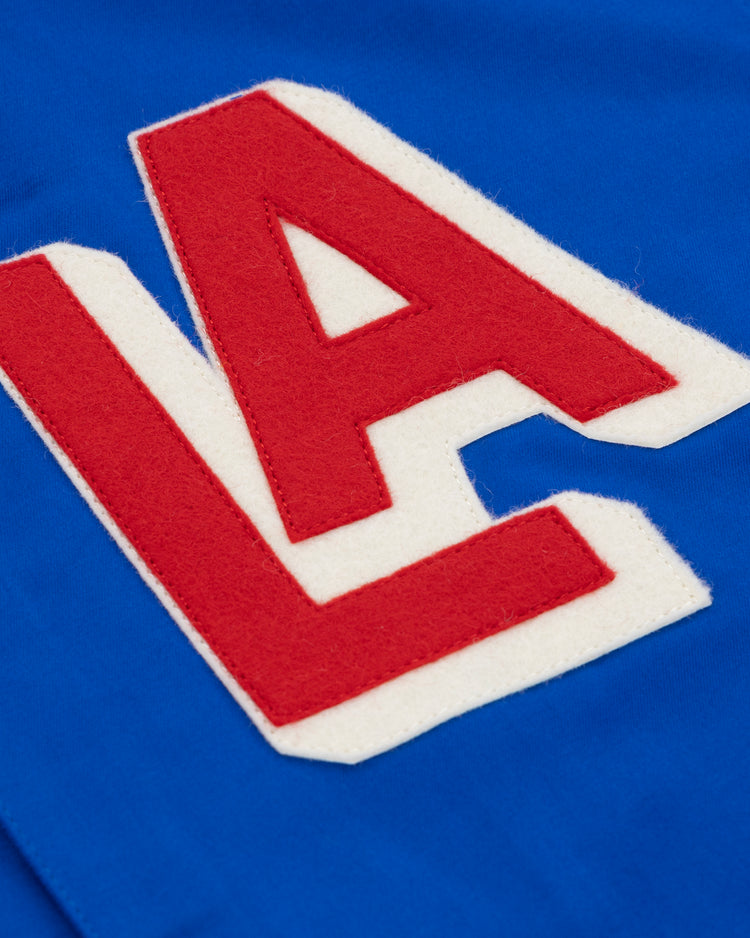 A close-up of blue fabric from the EFF Los Angeles (PCL) Satin Windbreaker featuring large red and white varsity LA letters, capturing vintage style and Pacific Coast League nostalgia.