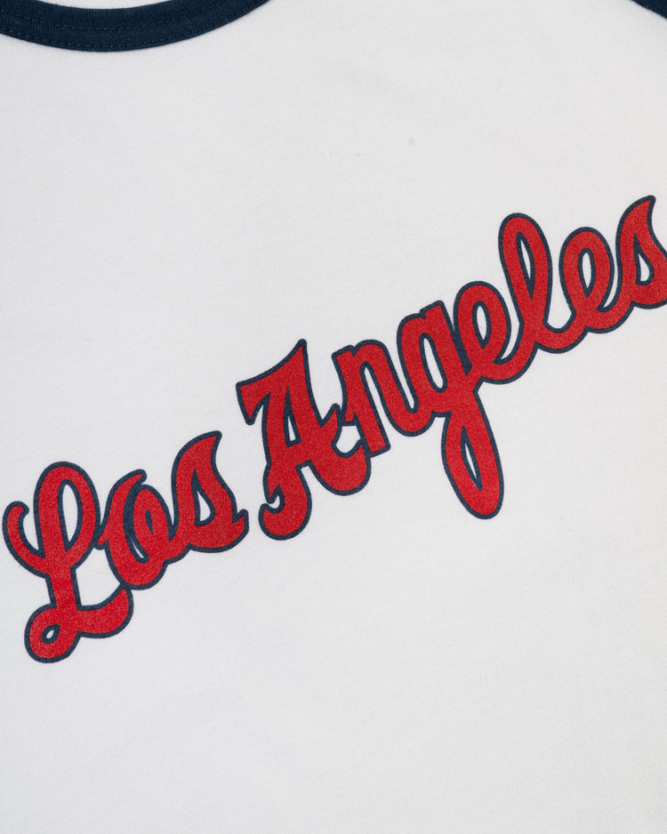A close-up of the Ebbets Field Los Angeles Angels (PCL) Vintage Baseball Tee showcases “Los Angeles” in large red cursive letters outlined in dark blue on a white shirt with a dark blue collar, evoking classic minor league style.