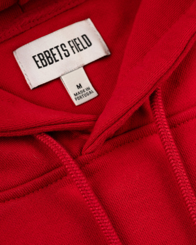 Close-up of the Los Angeles Angels (PCL) Heavyweight Cotton Terry Pullover Hoodie by Ebbets Field in red, size M, with a white Ebbets Field tag reading MADE IN PORTUGAL and detailed neckline stitching—classic vintage baseball style.