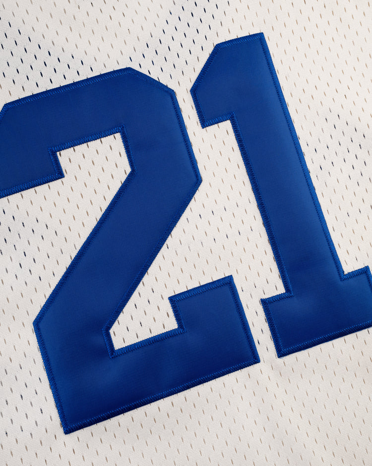 A close-up of the Ebbets Field Santurce Cangrejeros Mesh V-Neck Jersey features a large blue 21 stitched on white fabric, evoking the classic Roberto Clemente style.