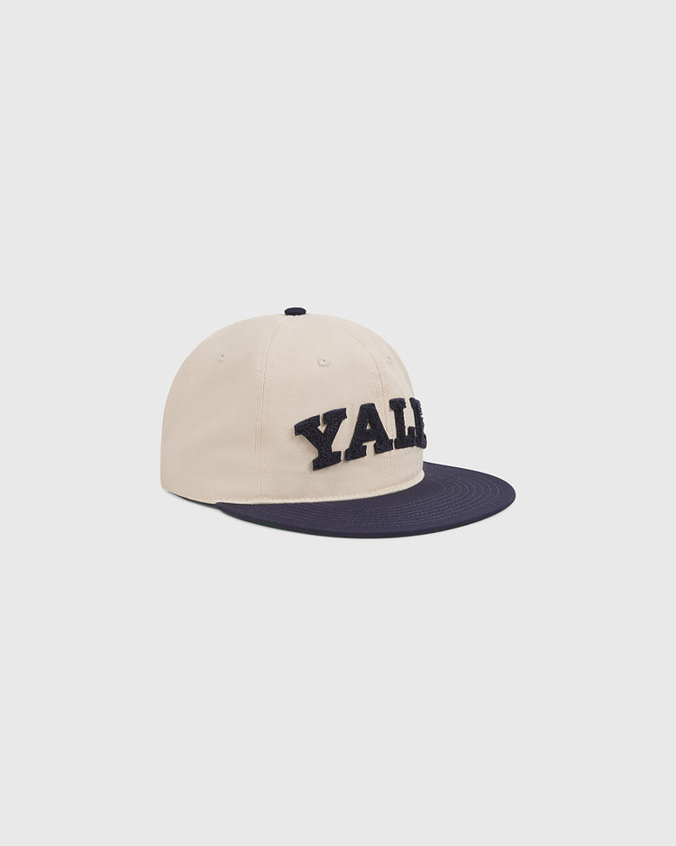 Showcase your Ivy League pride with the Yale Chenille Logo Cotton Twill Ballcap by Ebbets Field, featuring a beige cotton twill design, a navy blue brim, and “YALE” in large, bold navy chenille letters on the front—all displayed against a plain white background.