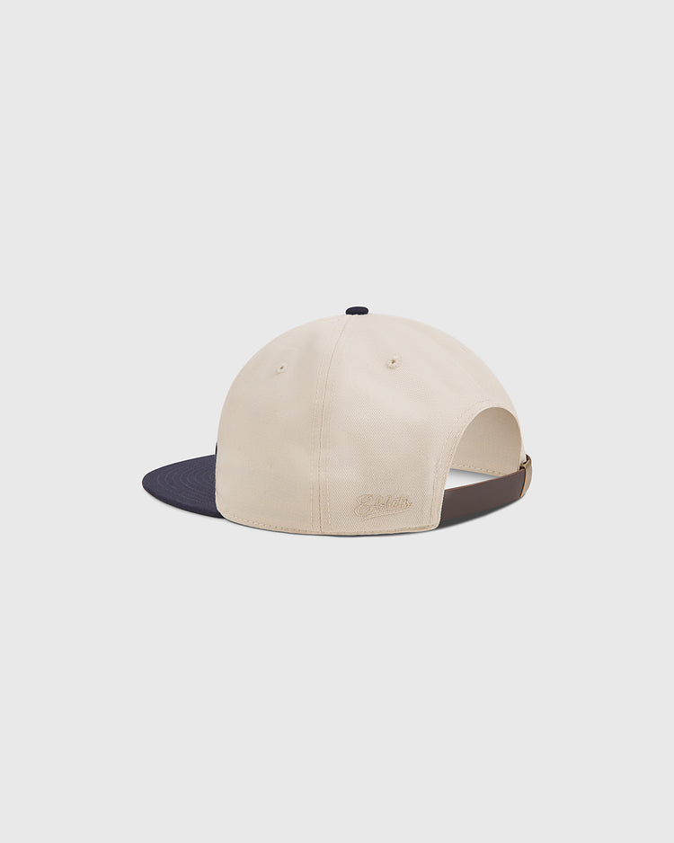 A beige Ebbets Field Yale Chenille Logo Cotton Twill Ballcap with a navy blue brim, shown from the back. The cap features an adjustable strap and subtle embroidered text above the opening, channeling classic Ivy League style.