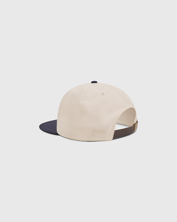 A beige cotton twill hat with a navy blue brim, shown from the back. The cap features a brown adjustable strap and subtle embroidered text above it, making this the classic Penn State Chenille Logo Cotton Twill Ballcap by Ebbets Field.