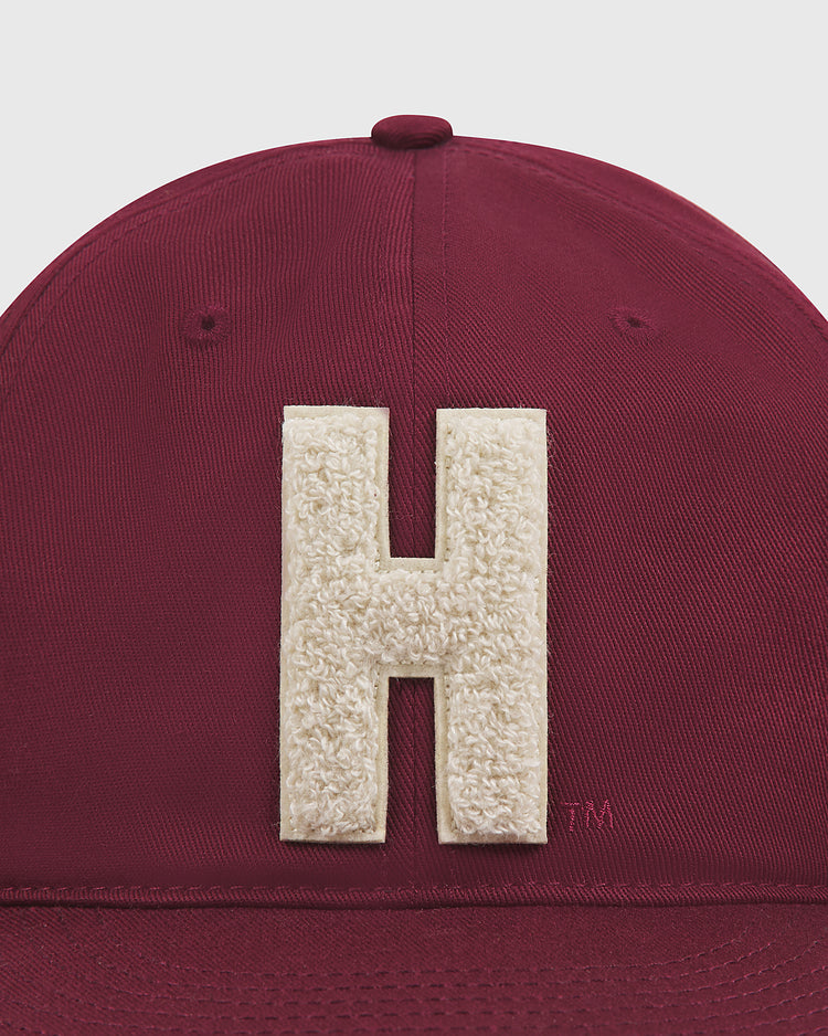 A close-up of the Ebbets Field Harvard University Chenille H Cotton Twill Ballcap, featuring a large, textured white “H” embroidered on the maroon front.