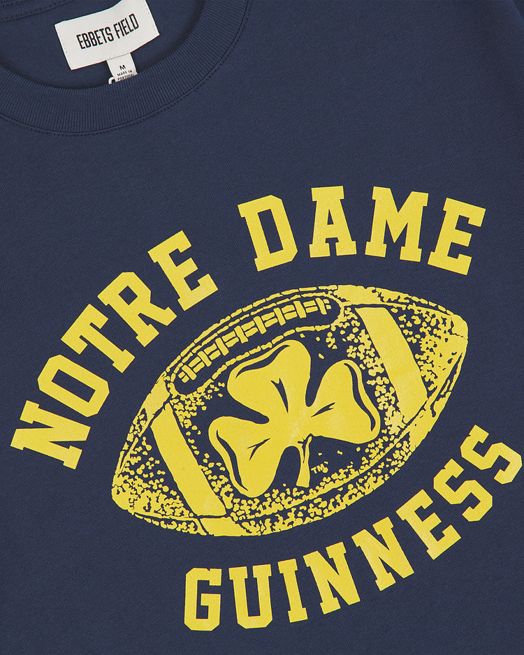 Show your Irish pride in the Ebbets Field Notre Dame X Guinness Short Sleeve Graphic Tee. This navy shirt features bold yellow NOTRE DAME GUINNESS text and a vintage-inspired football graphic with a shamrock at the center, blending classic collegiate spirit with retro style—perfect for any fan who wants to celebrate iconic Irish heritage.