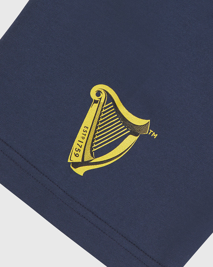 Show your Irish pride with the Notre Dame X Guinness Short Sleeve Graphic Tee by Ebbets Field, featuring a yellow harp logo and “estd 1759” printed on navy blue fabric. The partial view of the sleeve or hem against a light background makes it an ideal vintage-inspired tee for fans who appreciate Irish heritage.
