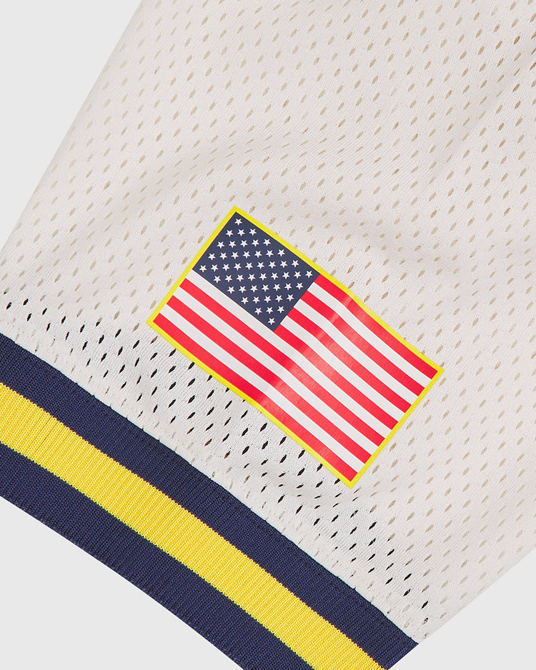 A close-up of the Ebbets Field US Naval Academy Mesh Football Jersey, featuring white mesh fabric, an American flag patch outlined in yellow, and navy and yellow striped trim at the bottom—a design that captures the classic style of a vintage football jersey.