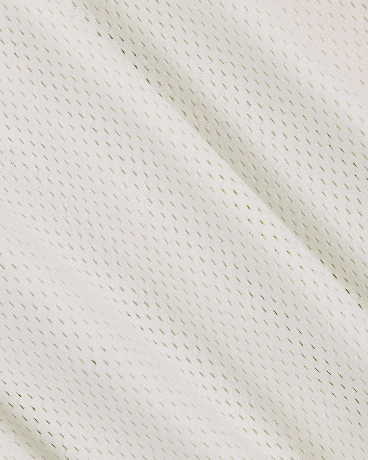 Close-up of the Ebbets Field US Naval Academy Mesh Football Jersey, featuring a white mesh fabric with small, evenly spaced holes that form a pattern of tiny dots reminiscent of classic football jerseys. The material appears soft and slightly draped, displaying gentle folds and subtle shadows.