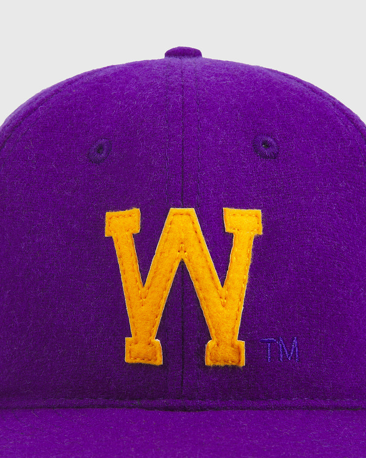A close-up of the University of Washington Authentic Wool Ball Cap by Ebbets Field, featuring a prominent yellow “W” stitched on the front of the purple wool cap and a small trademark symbol to the right.