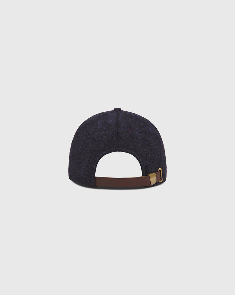 The Ebbets Field Notre Dame X Magee Irish Donegal Wool Ballcap is displayed from the back, highlighting its navy blue Donegal wool construction and a brown adjustable strap with a brass buckle, set against a plain light gray background.