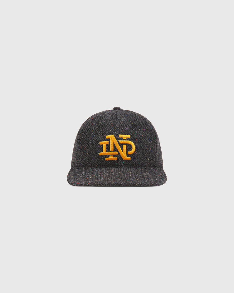 The Notre Dame X Magee Irish Donegal Wool Ballcap by Ebbets Field features a dark gray textured Donegal wool construction with a yellow embroidered ND logo on the front, shown against a plain light gray background.