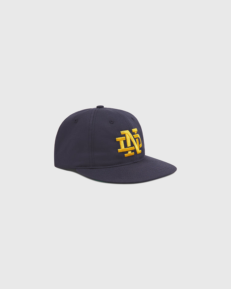 The Ebbets Field Notre Dame Cotton Ballcap, featuring a flat brim and yellow embroidered ND initials on the front, is shown against a plain light gray background.