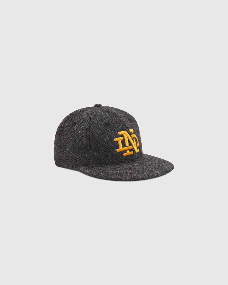 Notre Dame X Magee Irish Donegal Wool Ballcap by Ebbets Field in dark gray tweed, featuring yellow embroidered lettering on the front and a flat brim, displayed against a plain light gray background.