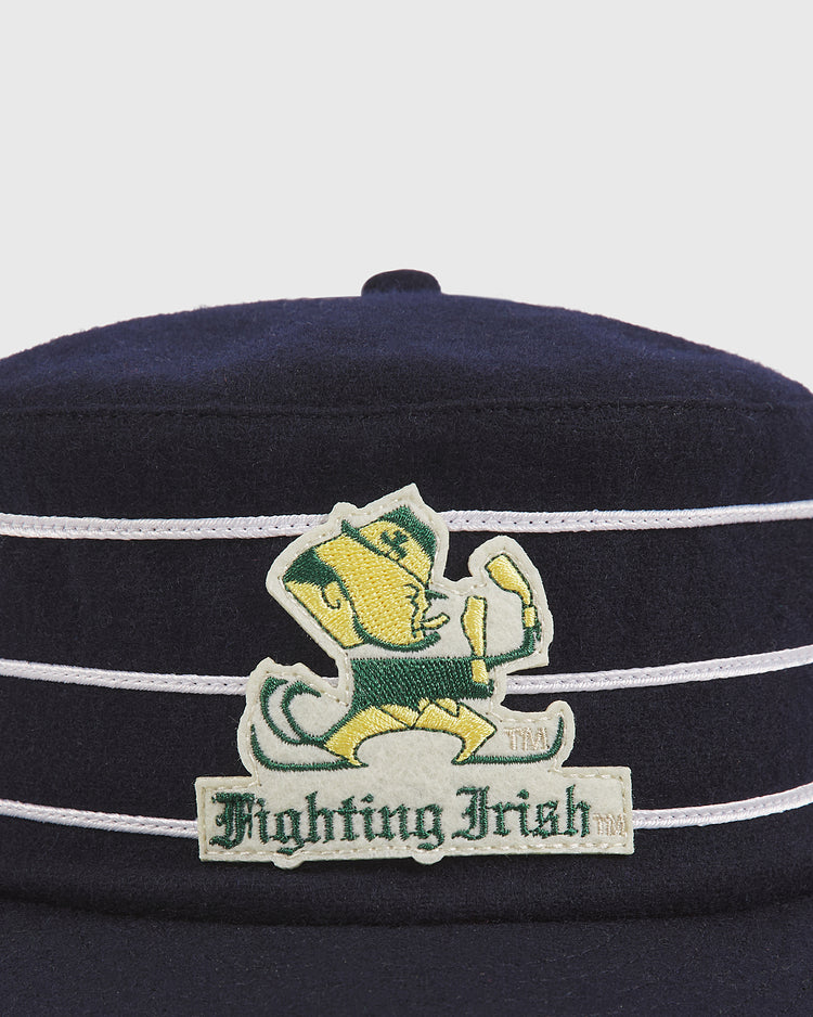 An Ebbets Field Notre Dame Pillbox Wool Ballcap in navy blue, featuring white stripes and an embroidered Fighting Irish leprechaun logo with raised fists on the front.