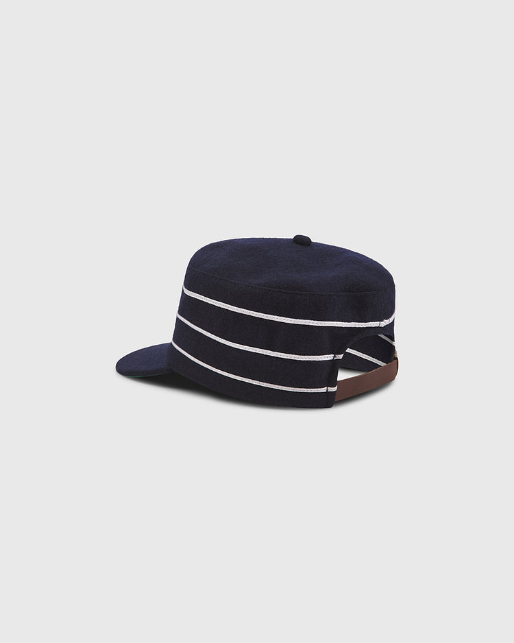A Notre Dame Pillbox Wool Ballcap by Ebbets Field, in dark blue with three white horizontal stripes and a short brim, featuring an adjustable brown strap at the back and shown against a plain light gray background.