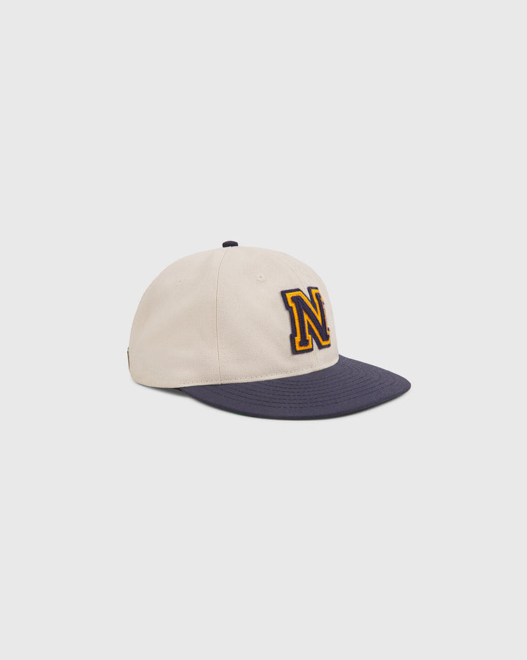 The Ebbets Field Navy 1958 Logo Cotton Twill Ballcap features a beige crown with a dark navy brim and a large yellow “N” outlined in black on the front, displayed on a plain light gray background.
