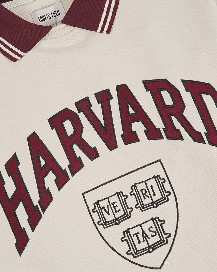 The Ebbets Field Harvard University Collared Crewneck Sweatshirt features a cream color with a maroon collar, bold “HARVARD” lettering in maroon, and the classic Harvard crest with “VERITAS” across three books.