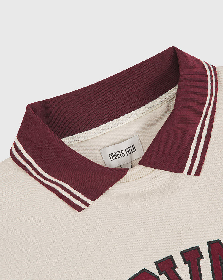 Close-up of the Harvard University Collard Crewneck Sweatshirt by Ebbets Field, featuring a cream color with a maroon and white striped collar; inner label shows Ebbets Field branding.