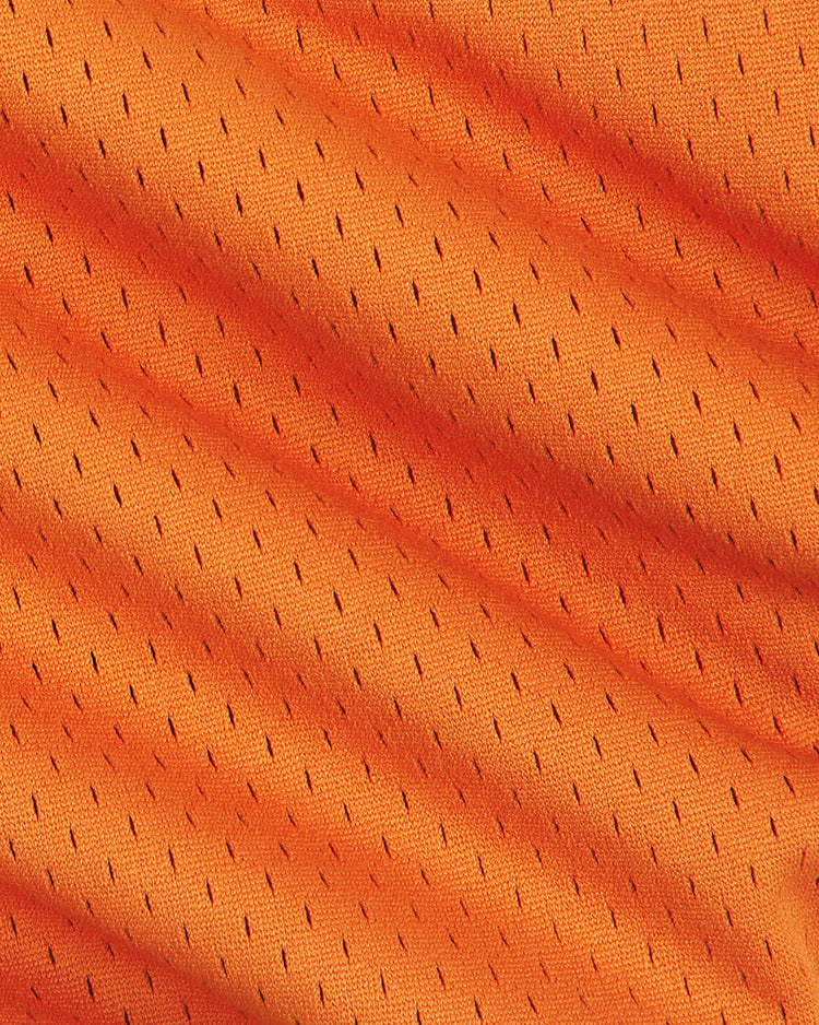 Close-up of orange mesh fabric from the University of Texas Mesh Football Jersey by Ebbets Field, featuring small, evenly spaced holes and gentle folds casting diagonal shadows—evoking the classic style worn by University of Texas athletes.