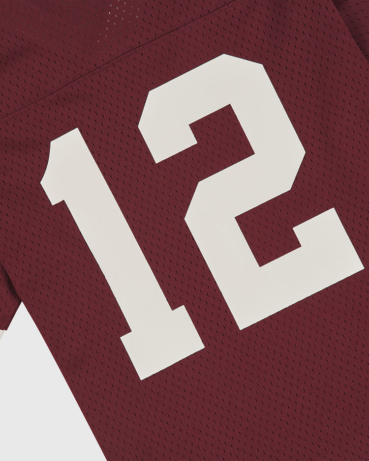 A close-up of the Ebbets Field Texas A&M Mesh Football Jersey showcases the textured vintage mesh fabric in maroon, featuring a large white number 12 and a partial view of the sleeve.