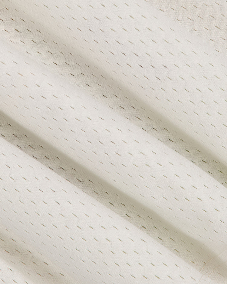 Close-up of the University of Washington Mesh Football Jersey by Ebbets Field, featuring white mesh fabric with evenly spaced, small perforated holes arranged in a grid pattern. The softly draped material forms gentle folds and subtle shadows—evoking the timeless look of classic Huskies jerseys seen in memorable Rose Bowl appearances.