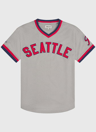 The Ebbets Field Seattle Rainiers 1951 Mesh V-Neck Road Jersey features SEATTLE in bold red and blue lettering across the chest, gray mesh fabric, navy and red trim on the sleeves and collar, and a small label at the neck.