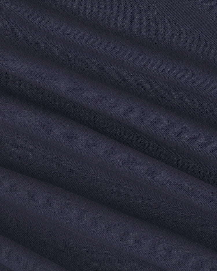 Close-up of the University of Michigan Collared Crewneck by Ebbets Field, showcasing dark blue fabric with horizontal, evenly spaced folds that create a soft, ridged texture. The material appears smooth and slightly matte, with subtle shading along the creases.