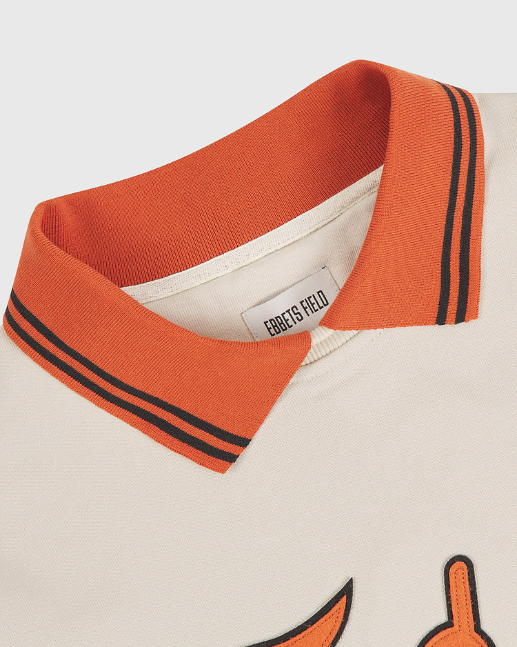 Close-up of the University of Texas Collared Crewneck by Ebbets Field: a cream shirt with an orange collar featuring black stripes. A white Ebbets Field tag is visible inside the collar, and part of an embroidered logo appears on the chest.