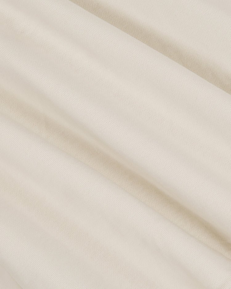 Close-up of the University of Texas Collared Crewneck by Ebbets Field, highlighting its light beige, soft fabric with subtle folds and a smooth texture that creates gentle shadows and a sense of depth across the surface.