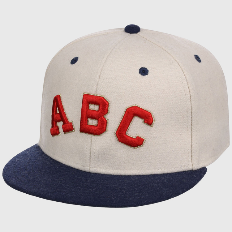 The Ebbets Field Atlanta Black Crackers NLB Ballpark Fitted Ballcap is beige with a dark blue brim and top button, featuring bold red “ABC” letters on the front.