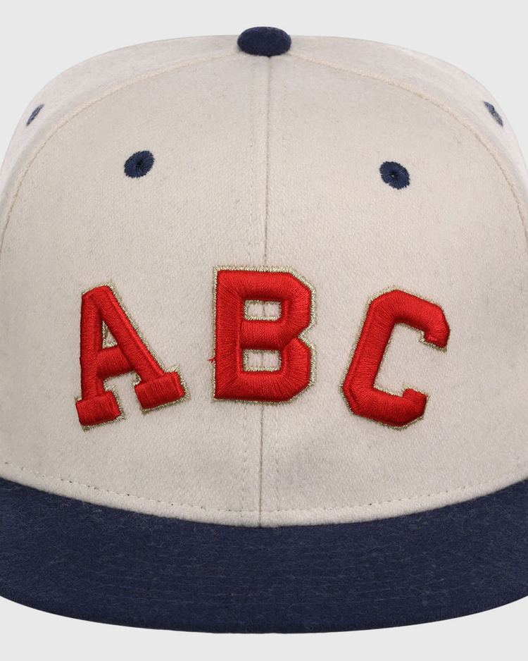 The Atlanta Black Crackers NLB Ballpark Fitted Ballcap by Ebbets Field is a beige cap with a dark blue brim, button, and eyelets, featuring large red 
