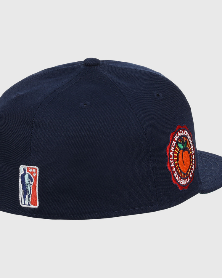 The EFF Atlanta Black Crackers NLB Team Color Fitted Ballcap is a vintage-inspired navy hat with a round orange and green side patch and a small man-with-bat embroidered logo on the back.