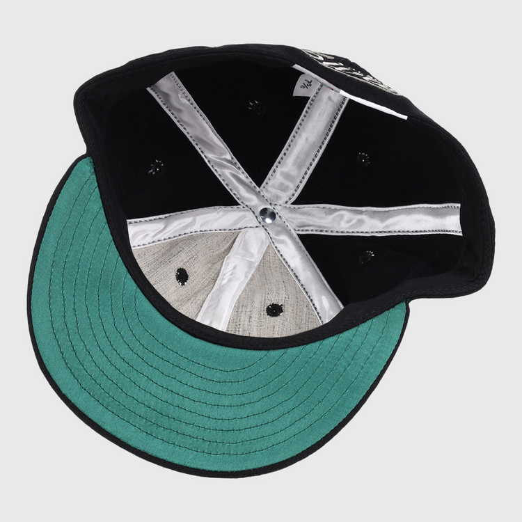 The image shows the inside of an Ebbets Field Flannels Black Fives Wool Ballcap, featuring a green underbrim, silver satin taping, center button, black ventilation holes, and a small white tag near the back.