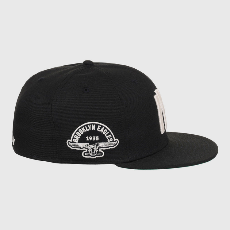 The Ebbets Field Brooklyn Eagles NLB Fitted Ballcap is a black cap with a flat brim, featuring “Brooklyn Eagles 1935” and an eagle graphic embroidered in white on the side.