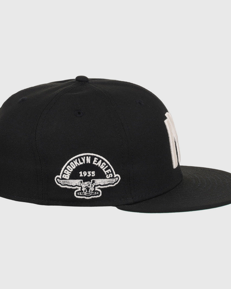 The Ebbets Field Brooklyn Eagles NLB Fitted Ballcap is a black cap with a flat brim, featuring “Brooklyn Eagles 1935” and an eagle graphic embroidered in white on the side.