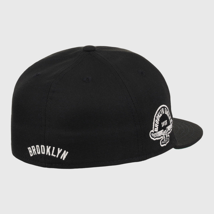 The Ebbets Field Brooklyn Eagles NLB Fitted Ballcap is a black, flat-brim cap featuring BROOKLYN embroidered in white on the back and a circular Brooklyn Eagles logo on the side panel above the ear.