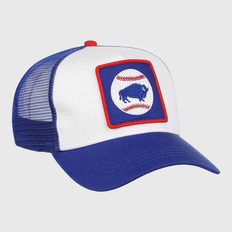 The Ebbets Field Buffalo Bisons MiLB Trucker Ballcap features a blue and white design with mesh back, plus a front patch showing a blue buffalo inside a red-bordered square, over two red baseball stitches on a white circle.
