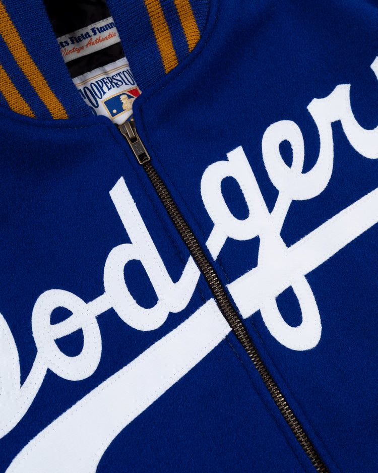 Close-up of the EFF Brooklyn Dodgers 1951 Authentic Wool & Leather Varsity Jacket in blue, featuring a yellow striped collar and white Dodgers script on the front, partially unzipped to show its retro inner tag.