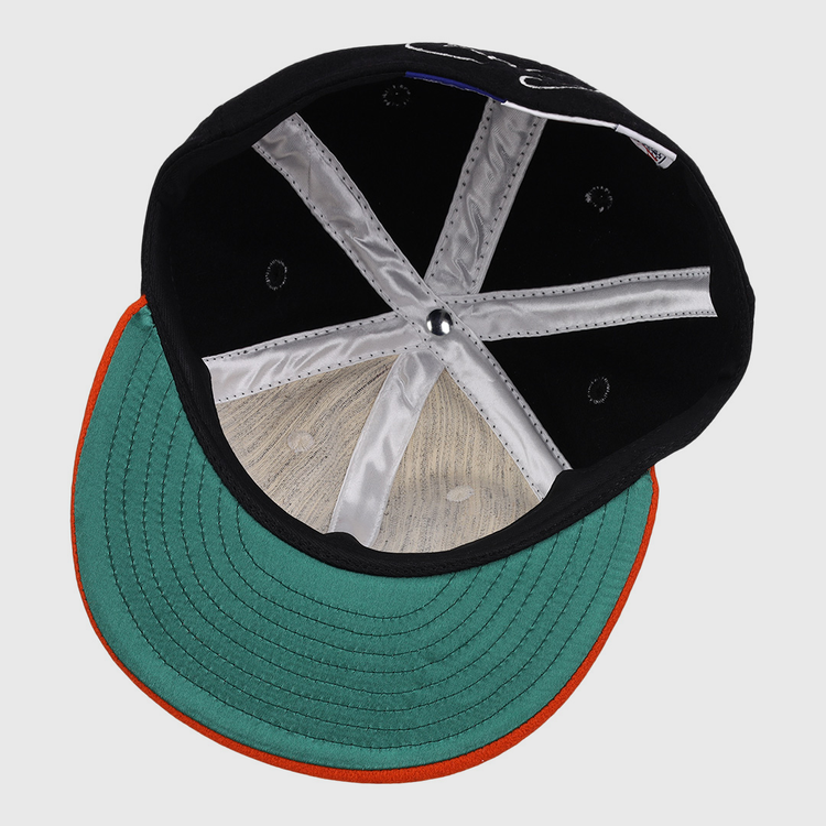 An overhead view of the Cal Ripken Jr. Signature Series Ballcap by Ebbets Field Flannels, featuring a green brim with an orange edge, visible inner stitching, silver panels, and a round button at the crown.
