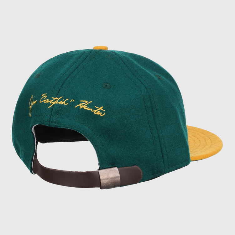 The Ebbets Field Flannels Catfish Hunter Signature Series Ballcap features vintage green wool, a yellow brim and button, yellow script embroidery on the back, and an adjustable brown strap with metal clasp.