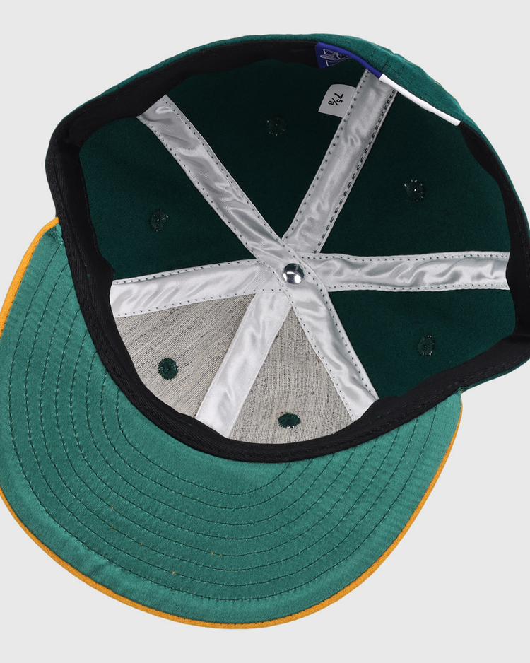 Inside view of the Ebbets Field Flannels Catfish Hunter Signature Series Ballcap, featuring a green crown, yellow brim, white stitching, fabric tag, and six ventilation holes.
