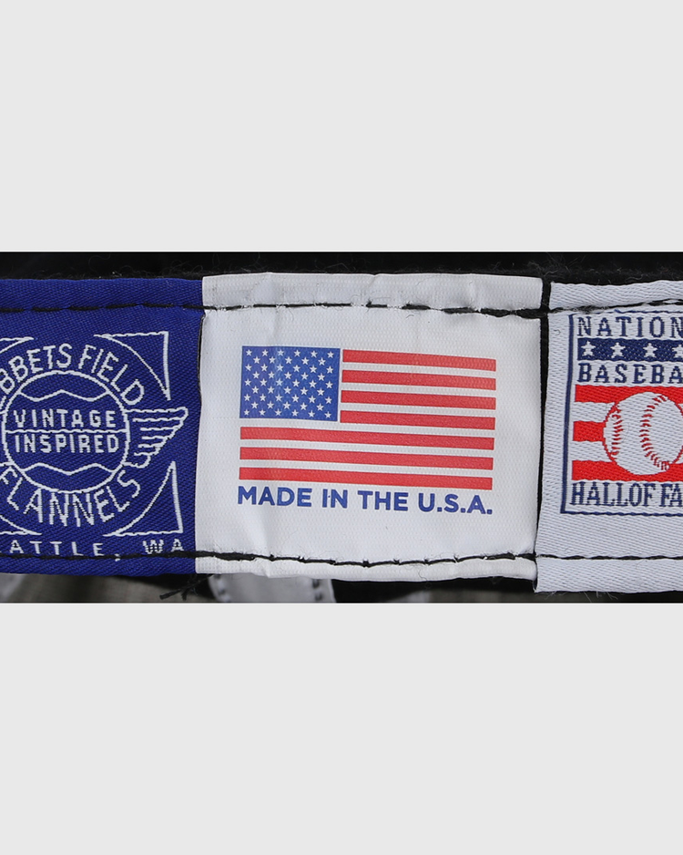 The Catfish Hunter Signature Series Ballcap by Ebbets Field Flannels features three fabric labels: Ebbets Field Flannels Vintage Inspired Seattle, WA; a U.S. flag with Made in the U.S.A.; and National Baseball Hall of Fame.
