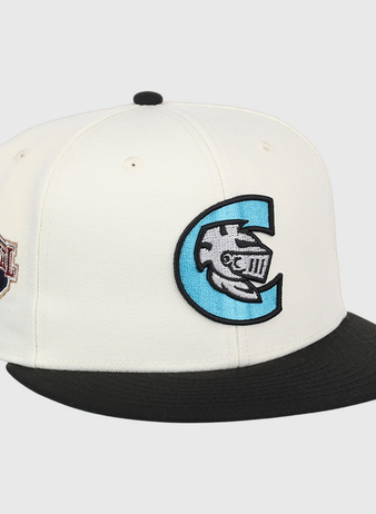The Ebbets Field Charlotte Knights MiLB Snapback Ballcap is a white cap with a black brim, a large blue and black C logo with a fish and Roman numerals on the front, plus a brown Continental League patch on the side.