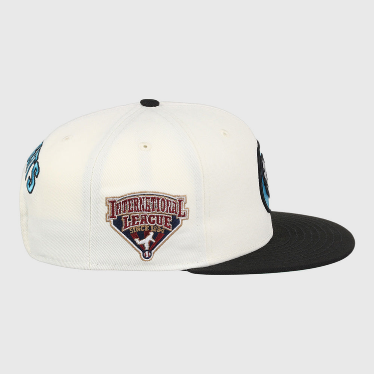 The Ebbets Field Charlotte Knights MiLB Snapback Ballcap is a black and white cap, shown from the side, featuring an International League Since 1884 patch with a red and white shield on the side panel.